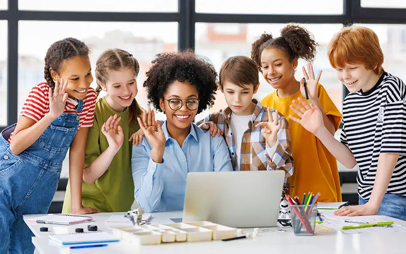 teacher and students waving to a computer